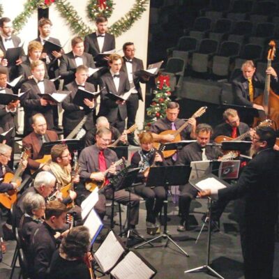 A group of people in tuxedos and tuxedos standing in front of a christmas tree.
