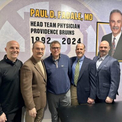 Group of five men in front of sign.
