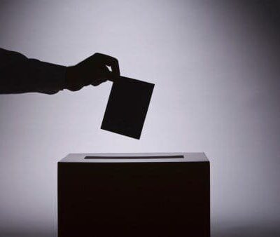 A person putting a voting card into a voting box.