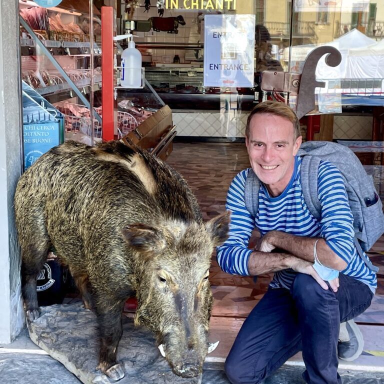 A man kneeling next to a boar in front of a shop.
