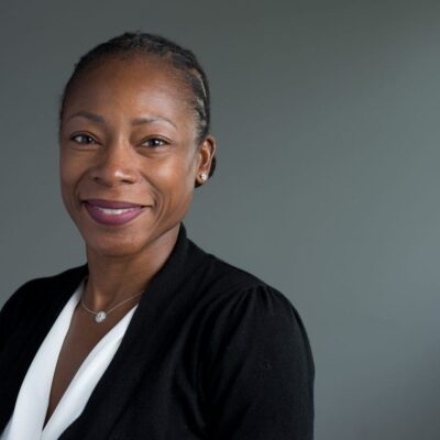 A woman in black jacket standing next to wall.