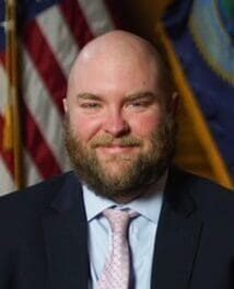 An Attorney General in a suit and tie in front of an American flag.