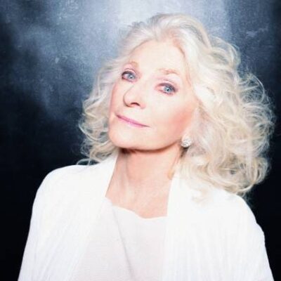 A woman with white hair posing in front of a black background.