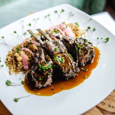 Lamb chops on a white plate with sauce.