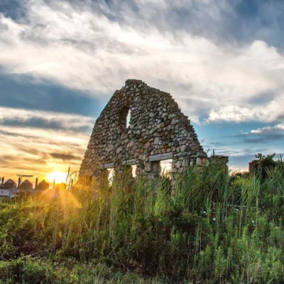 An old stone building with a sun setting behind it.
