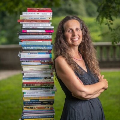 Woman standing with a stack of books.