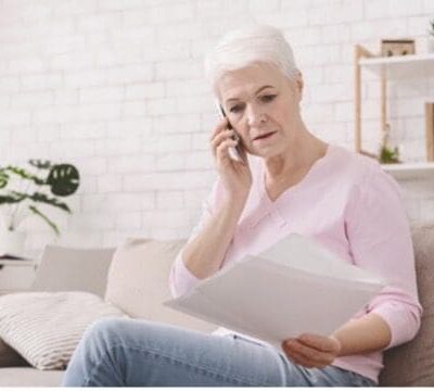 An older woman sitting on a couch and talking on the phone.