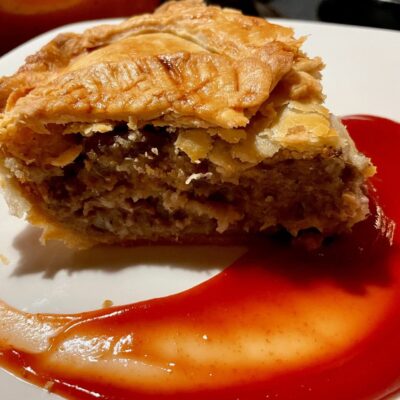 A piece of meat pie with sauce on a plate.
