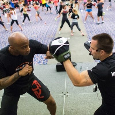 Two men engaged in a self-defense workout session at a gym.