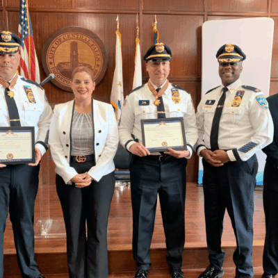 Four police officers holding certificates in front of a stage.