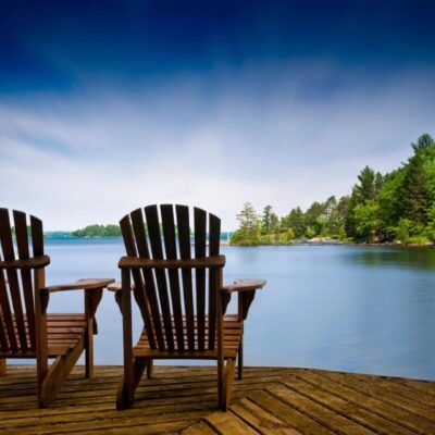 Two Adirondack chairs overlooking a lake.
