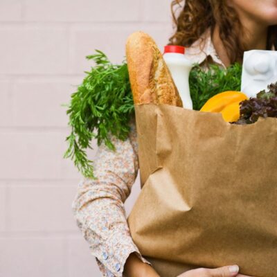 A woman holding a shopping bag full of groceries.