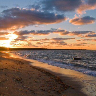 The sun is setting over a sandy beach and water.