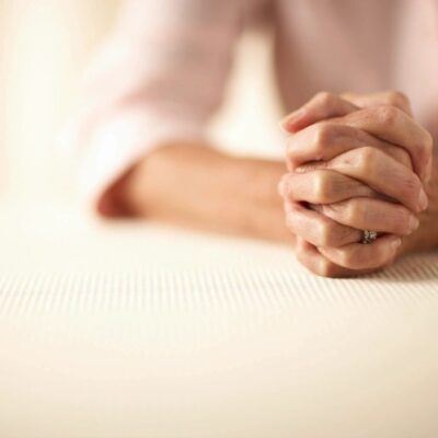 A woman is sitting on a table with her hands clasped.
