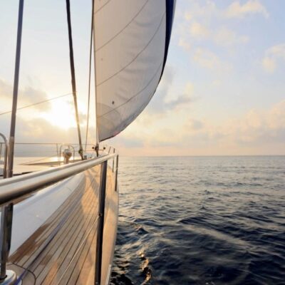 Sailboat cruising on calm ocean waters during sunset.