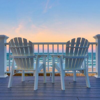 Two adirondack chairs on a deck overlooking the ocean.