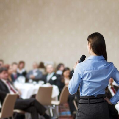 A business woman giving a speech in front of an audience.