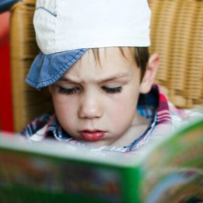 A young boy wearing a hat reading a book.