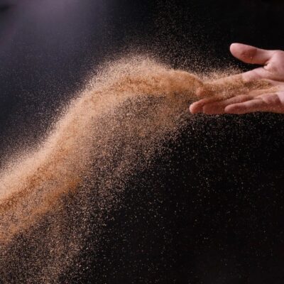 A person's hand is throwing sand onto a black background.