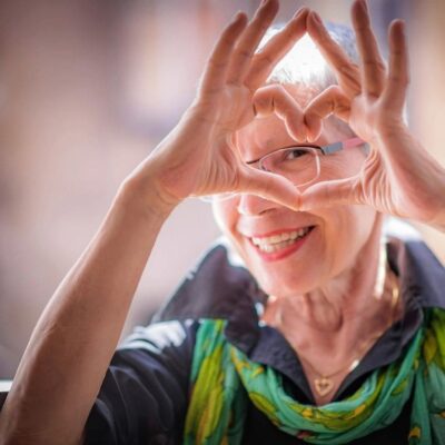 Smiling elderly woman making a heart shape with her hands.