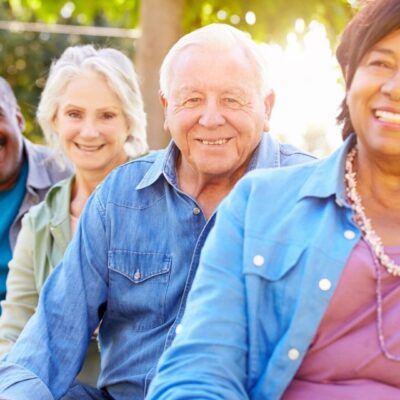 A group of older people sitting on a bench and smiling.