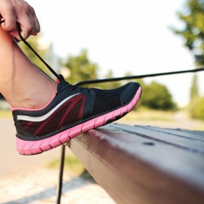 A woman is tying her shoes on a bench.