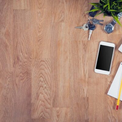 Laptop, phone, keys, notepad on wood desk.