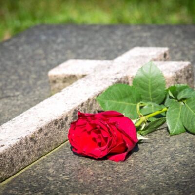A red rose sits on top of a gravestone.