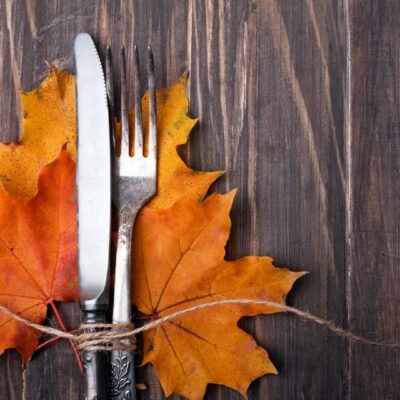 A fork, knife and autumn leaves on a wooden table.