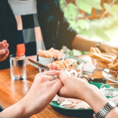 A group of people holding hands at a table with food.