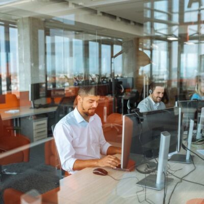 Two men working at computers in a modern office separated by glass partitions.