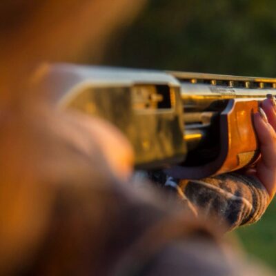 Person aiming shotgun at sunset.