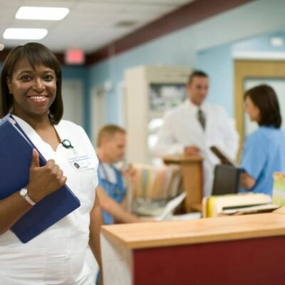 Smiling nurse holding patient files at desk.