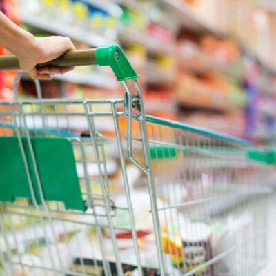 A person pushing a cart in the aisle of a grocery store.