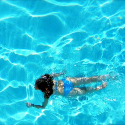 A woman in a blue bikini swimming in a blue pool.