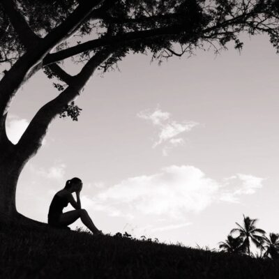 Silhouette of person sitting under a tree.