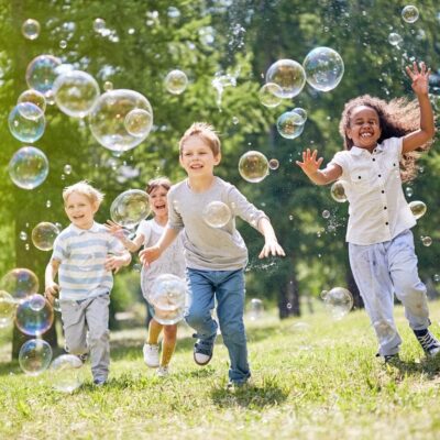 Kids chase bubbles in a park.