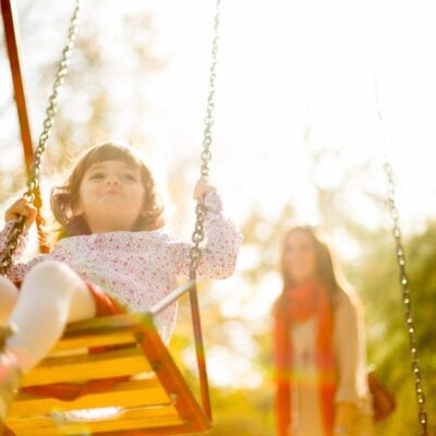 A little girl on a swing with her mother.