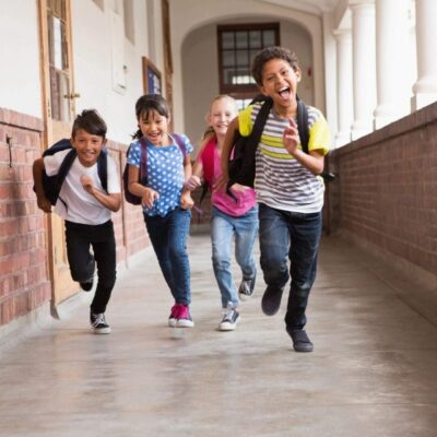Happy kids running down school hallway.