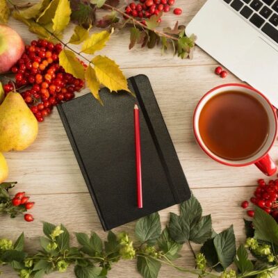 A cozy workspace with a notebook, pencil, tea, and autumn leaves.