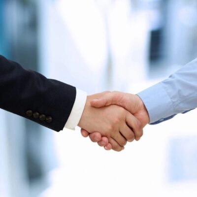 Two businessmen shaking hands in front of a blurred background.