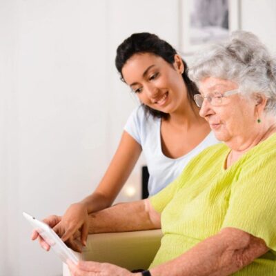 Young woman helps elderly woman with tablet.