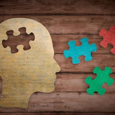 Wooden head silhouette with colorful puzzle pieces on wooden background.