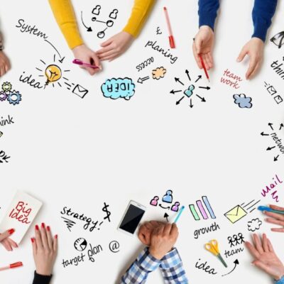 A group of people holding hands around a white table with doodles on it.