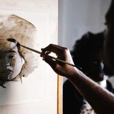 A man is painting a portrait of a woman on a easel.