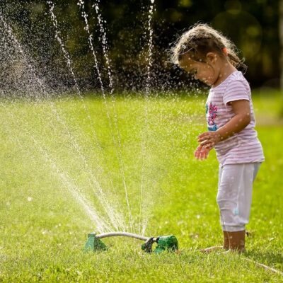 A little girl playing with a sprinkler in the grass.