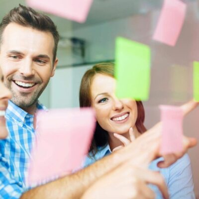 A group of people looking at sticky notes on a glass wall.