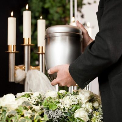 Person holding urn, candles, flowers.