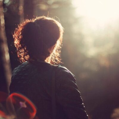 Woman in jacket facing sunlight in woods.