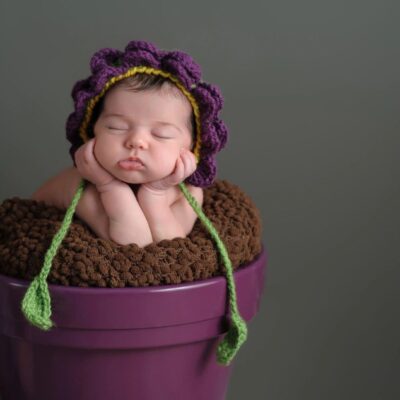 A baby sleeping in a purple pot with a knitted hat.
